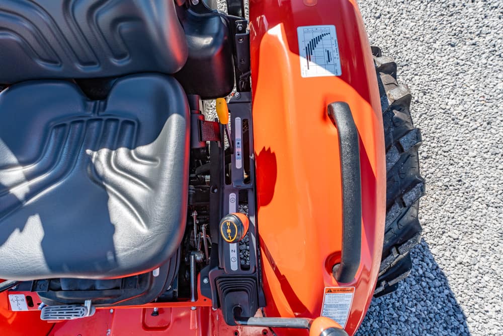 Top-down view of an orange tractor cab showing the seat, gear shift, and a large rear tire on gravel
