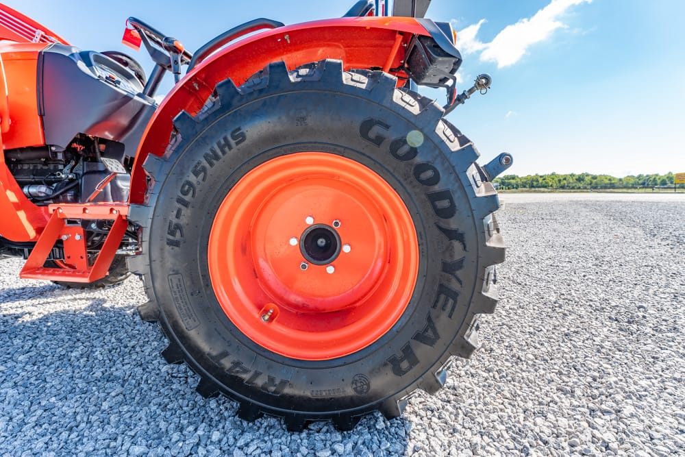Close-up of a bright orange tractor wheel and large Goodyear tire on a gravel surface under a clear blue sky.