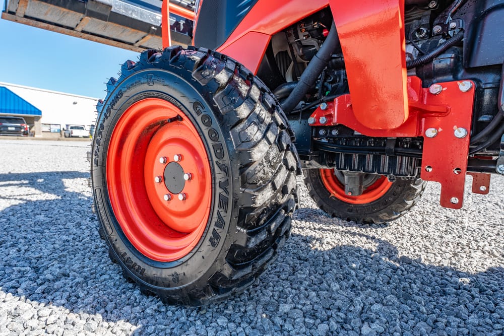 Close-up of a red tractor wheel with a rugged Goodyear tire on a gravel surface, part of the orange machinery frame visible.