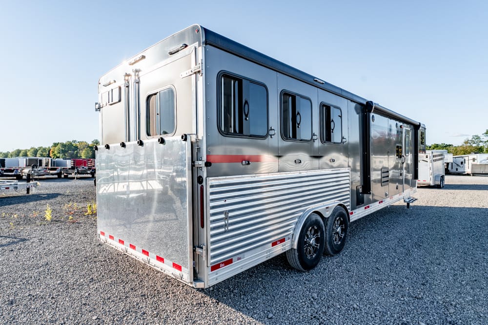Silver aluminum double-axle horse trailer with side windows parked on gravel.