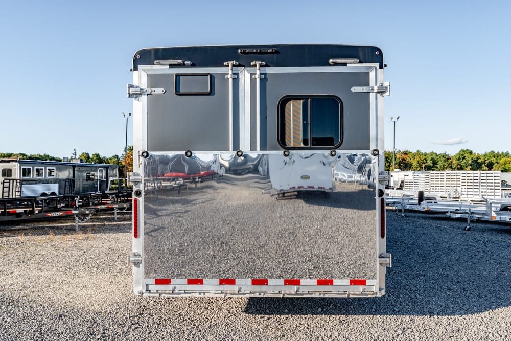 Rear view of a shiny aluminum trailer in a lot with other trailers on gravel ground.