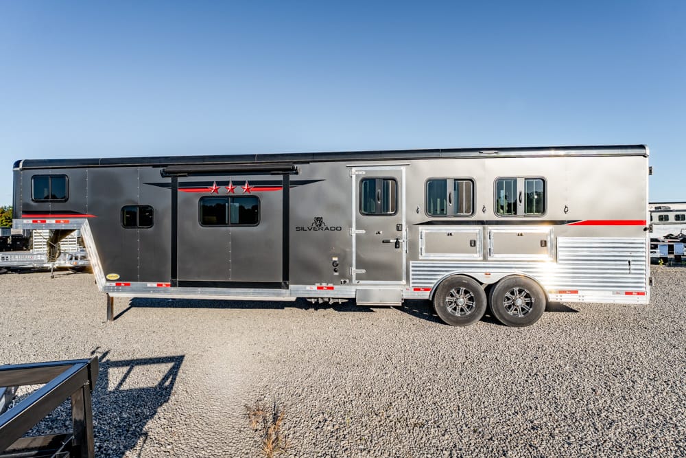 Silver Silverado horse trailer with a black front door, red stripe and three red stars, parked on gravel.