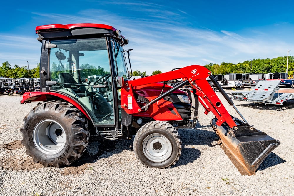 Red tractor with a front loader bucket parked on gravel, clear blue sky above, in a equipment lot.