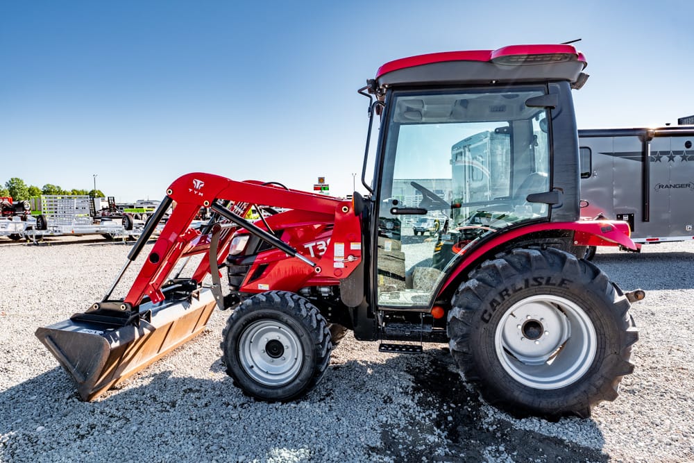 Red compact tractor with a front-end loader parked on a gravel lot, under a clear blue sky.
