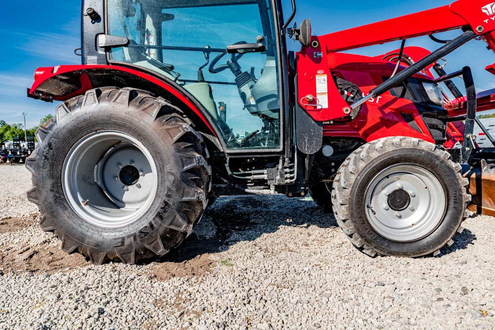 Red agricultural tractor with enclosed cab and front loader on a gravel lot under a blue sky