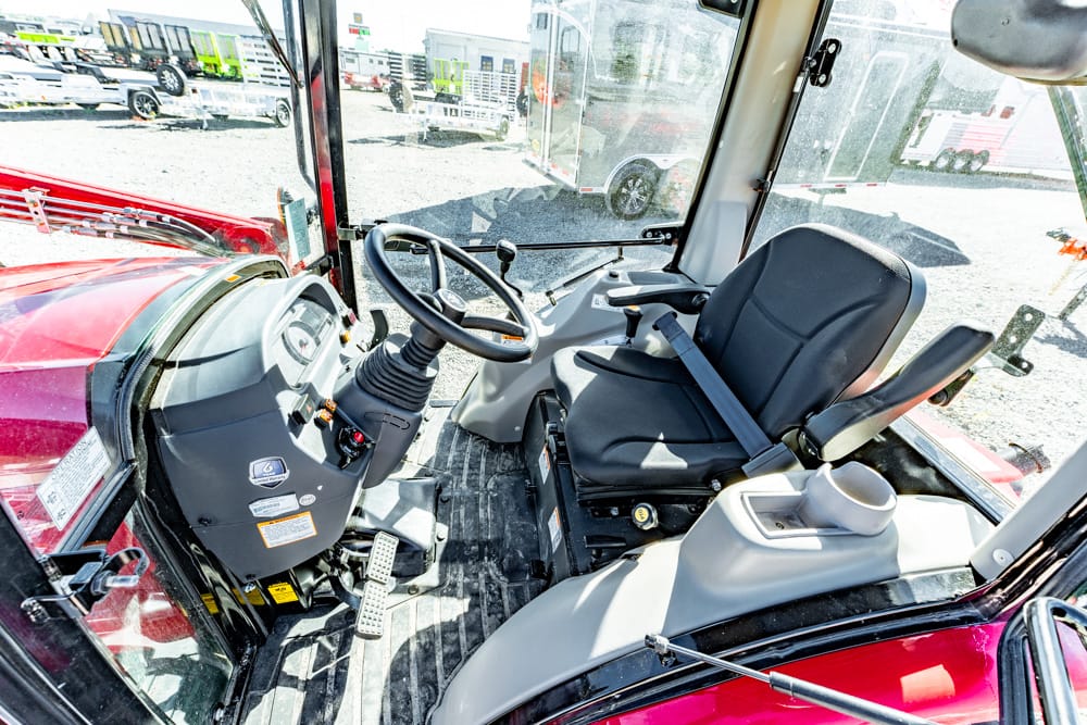 Interior of a red tractor cab showing the steering wheel, operator seat, and pedals