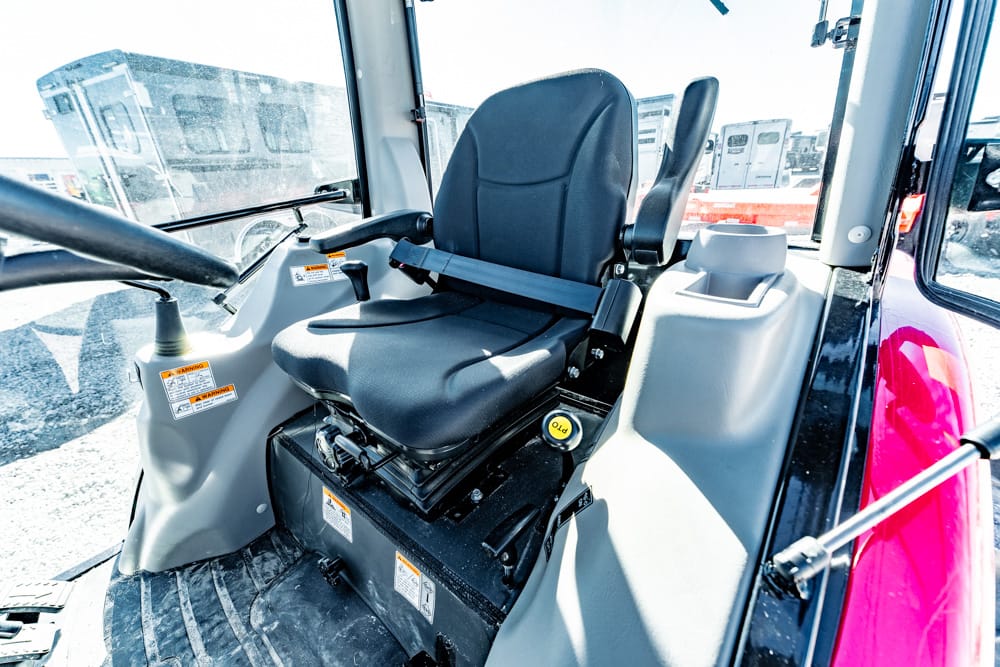 Interior of a construction vehicle cab with a black operator seat and safety belt, surrounded by controls and windows