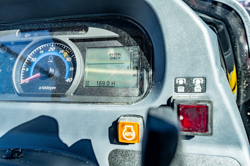 Close-up of a vehicle dashboard: round speedometer, digital display reading 169.0 H, and an orange AUTO button nearby.
