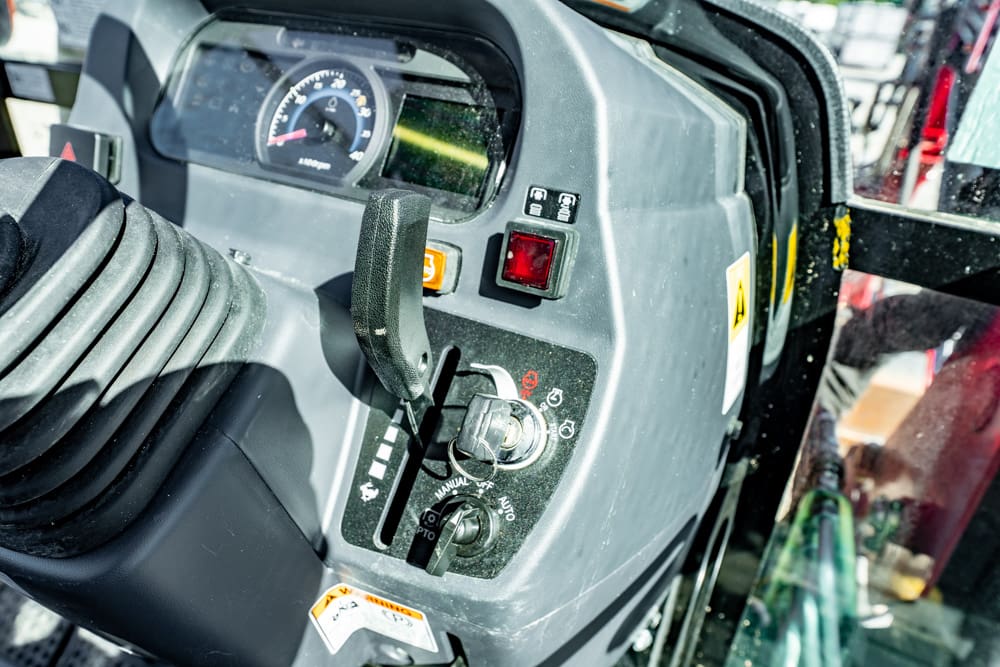 Close-up of a heavy machinery control panel showing a joystick, gauge, and switches in a cab setting
