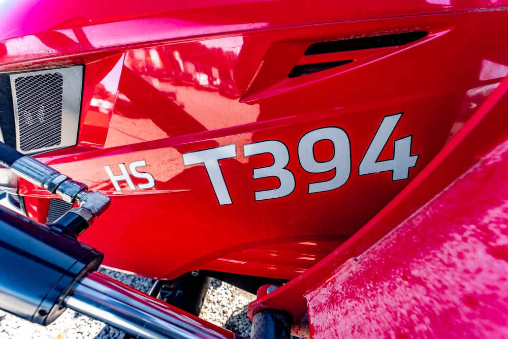 Close-up of a bright red vehicle panel with the white letters 'HS' and the code 'T394'. A chrome handlebar/hose is in the foreground.