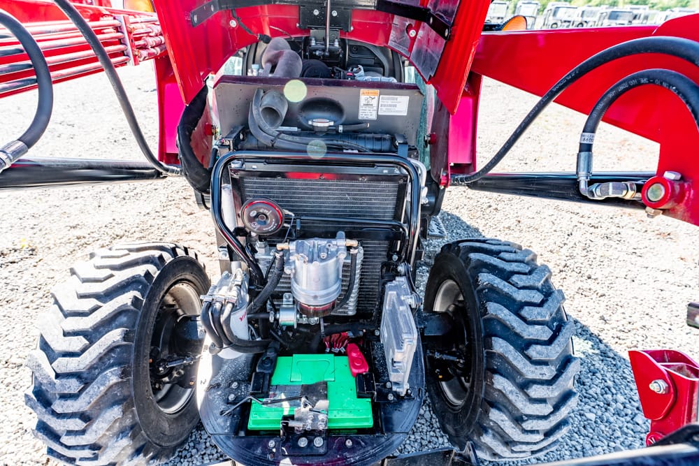 Open engine bay of a red tractor showing radiator, belts, and a green battery pack at the base.