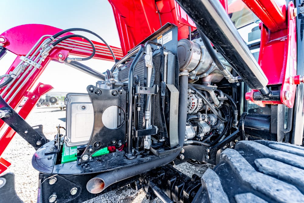 Open hood reveals a red tractor engine with belts, hoses, and metal components exposed for maintenance area detail.
