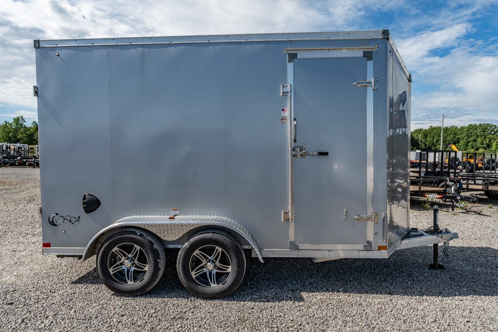 Gray enclosed cargo trailer with two axles and diamond-plate fenders on a gravel lot