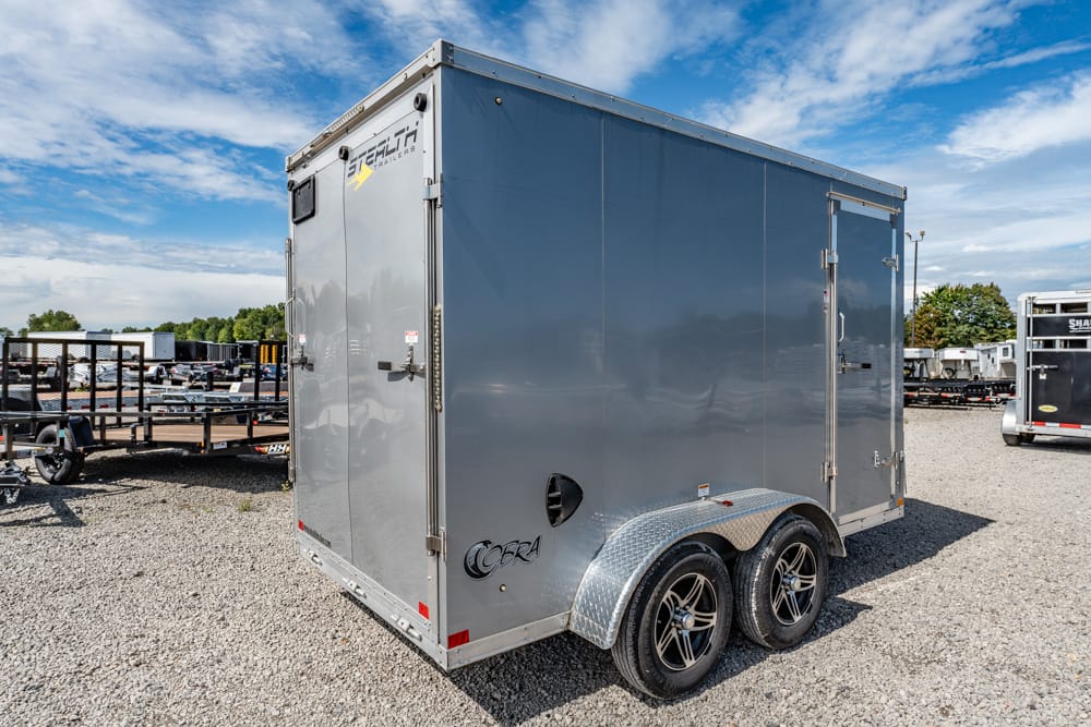 Gray enclosed cargo trailer with dual axles and diamond-plate fenders in a gravel lot for trailer storage or sale background
