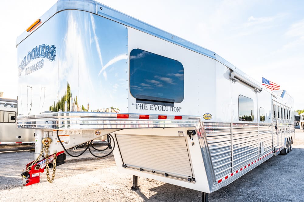 Large silver fifth-wheel RV trailer on a gravel lot, labeled 'The Evolution' with an American flag nearby.