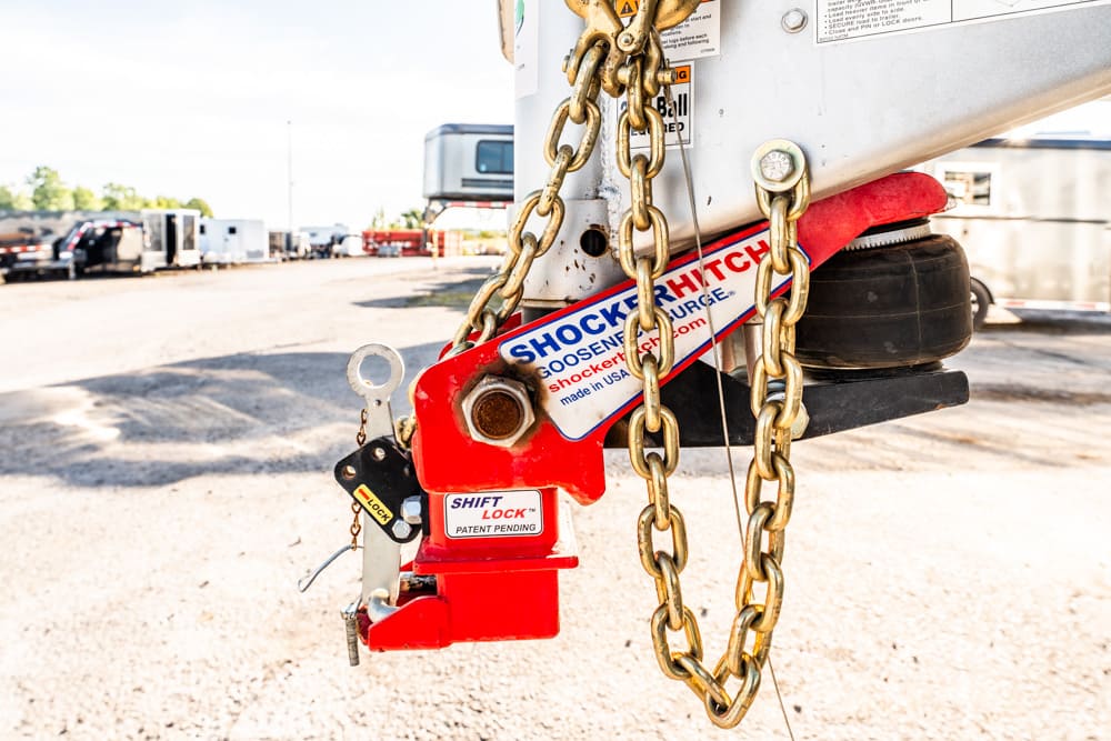 Close-up of a red trailer hitch lock securing a hitch with heavy gold chains in a dusty lot, preventing movement.