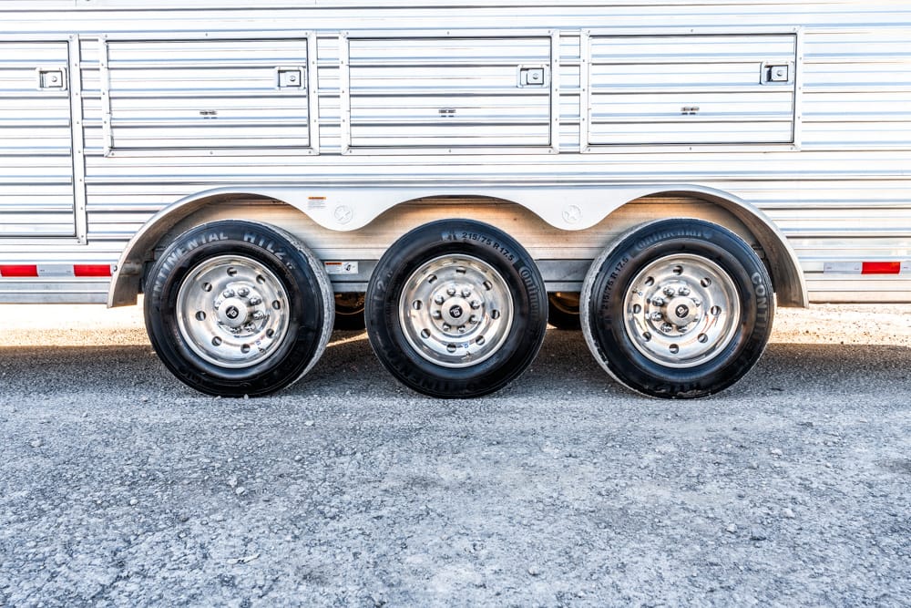Triple-axle trailer with silver wheels and curved fenders on a gravel road