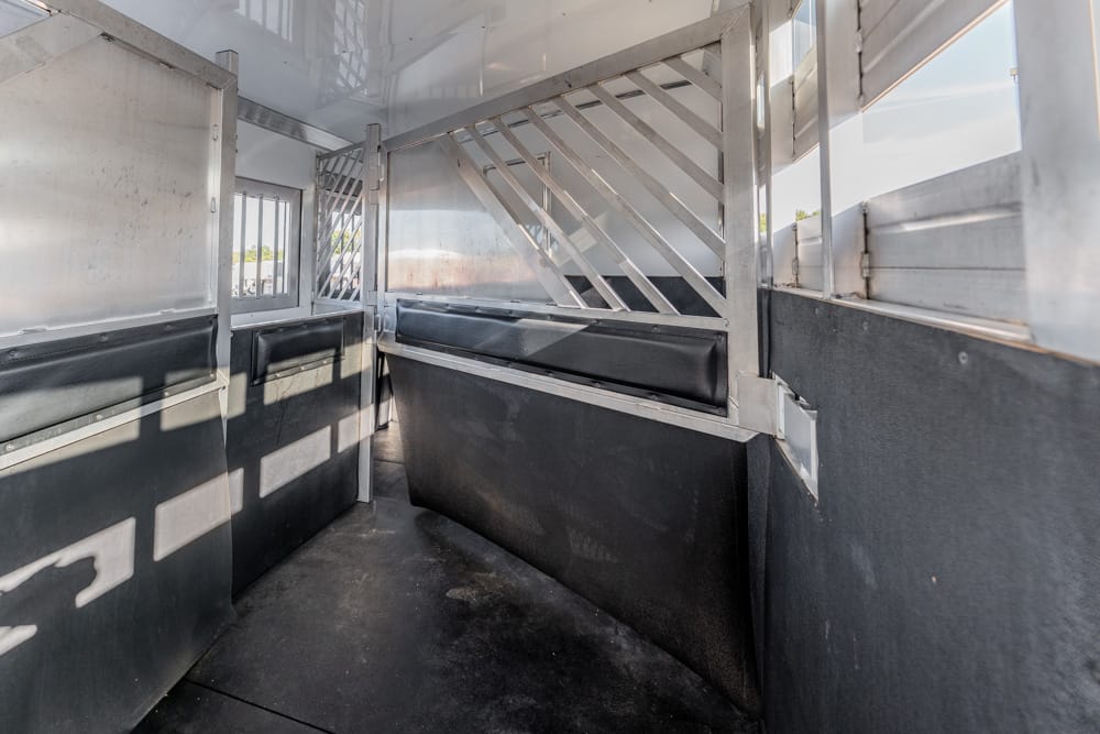 Interior of a metal livestock trailer with partition bars and padded walls, ready to transport animals on a sunny day