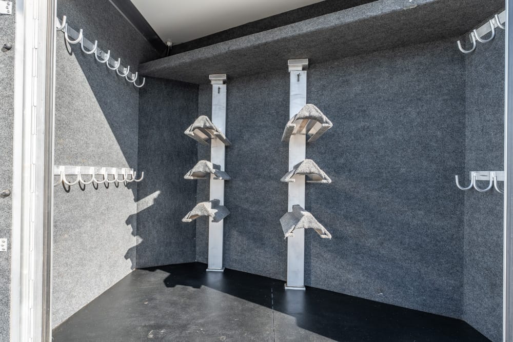 Interior of a utility trailer with metal angled racks on vertical supports and rows of wall hooks on both sides
