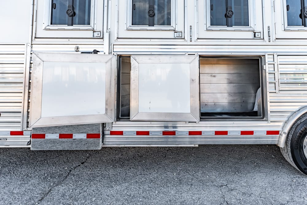 Silver trailer side with two large storage compartments, one open, showing metal interior and wheel nearby