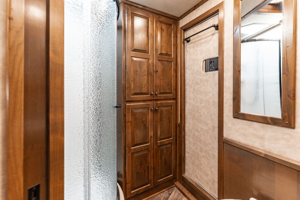 Wooden cabinet storage and a frosted shower door inside a small bathroom, with a framed mirror on the wall.