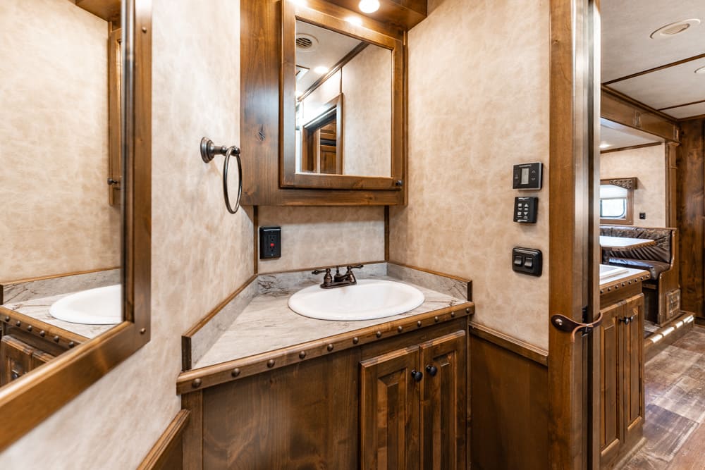RV bathroom vanity with marble countertop, white sink, and wood-framed mirror in a luxury trailer.