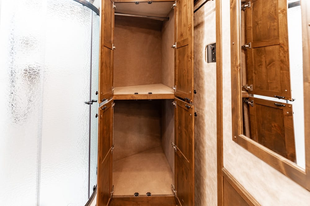 Open wooden bathroom cabinet with two shelves beside a frosted curved shower door.