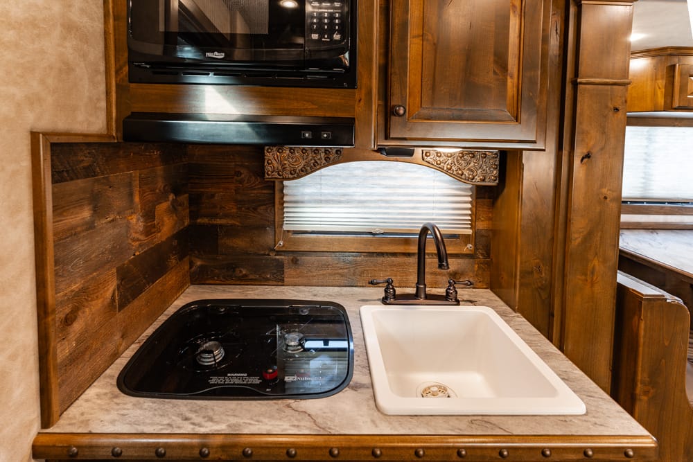 Compact RV kitchen with dark wood cabinets, black glass stovetop, and white undermount sink.