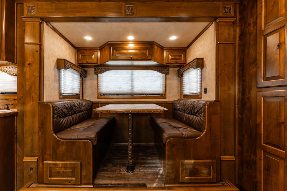 Wood-paneled camper dining booth with brown leather benches and a central rectangular table.