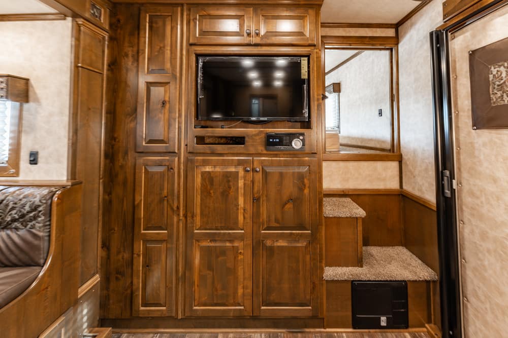 RV living area with dark wood cabinets, mounted TV, and built-in storage center across from a small staircase to a carpeted step-up area