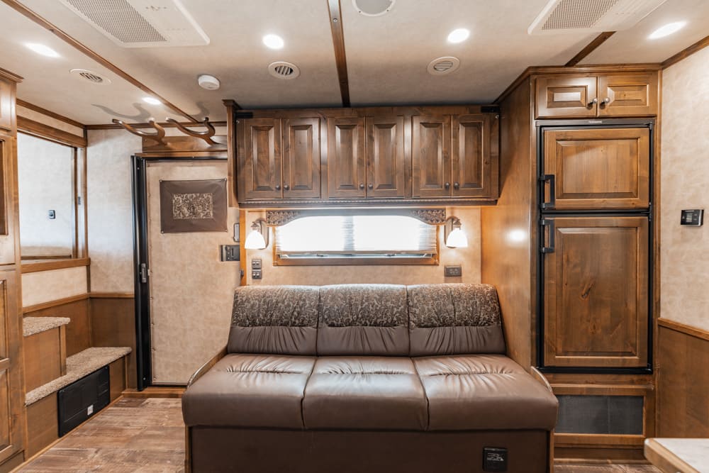 Wood-paneled RV interior with a brown leather sofa, overhead cabinets, and a full-size fridge on the right; cozy living space with warm lighting.