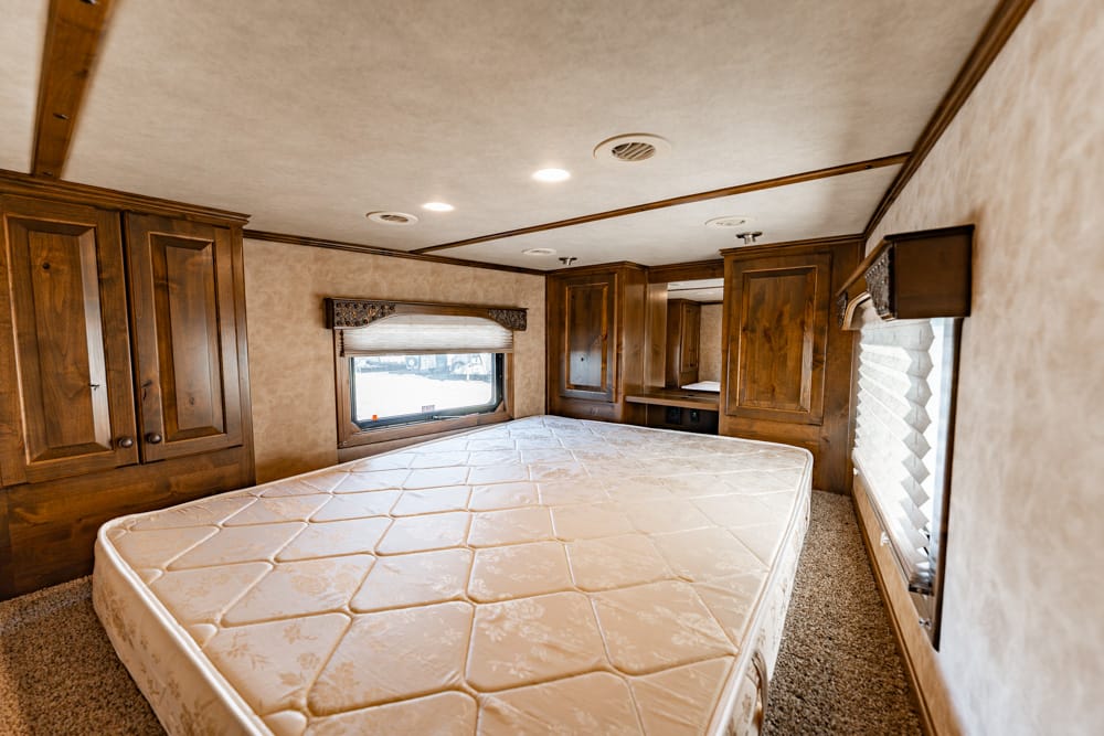 Wood-paneled RV bedroom with a large mattress and built-in cabinets along the walls