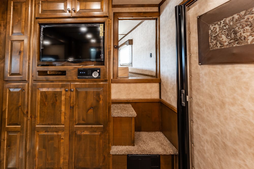 Wood-paneled RV interior with a mounted flat-screen TV, storage cabinets, and carpeted steps leading to a small upper area