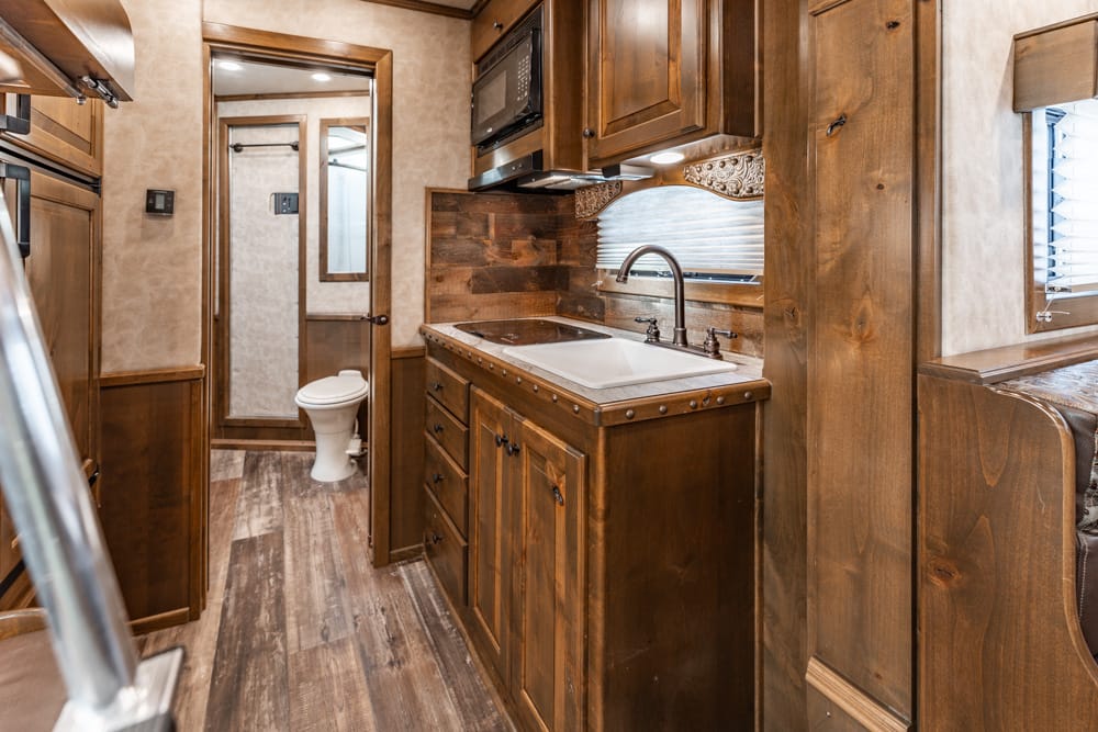 Wood-paneled RV kitchen with white sink, dark cabinets, and a doorway to a small bathroom at the back of the space.