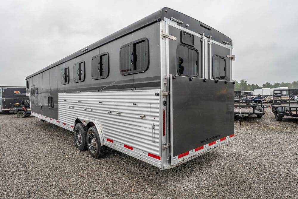Long gray aluminum horse trailer with multiple windows, parked on a gravel lot under overcast skies