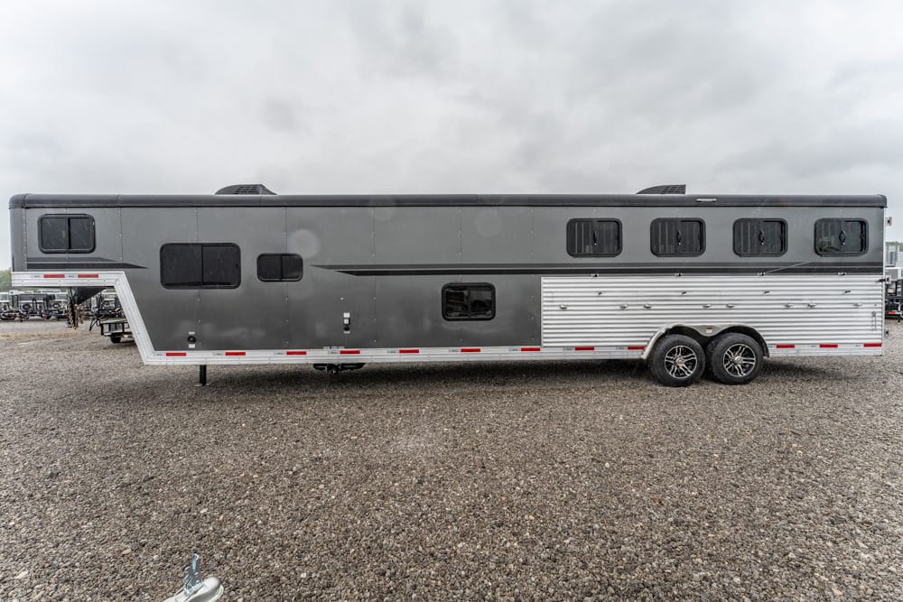 Long gray and silver double-axle travel trailer parked on a gravel lot, with multiple windows along its side.