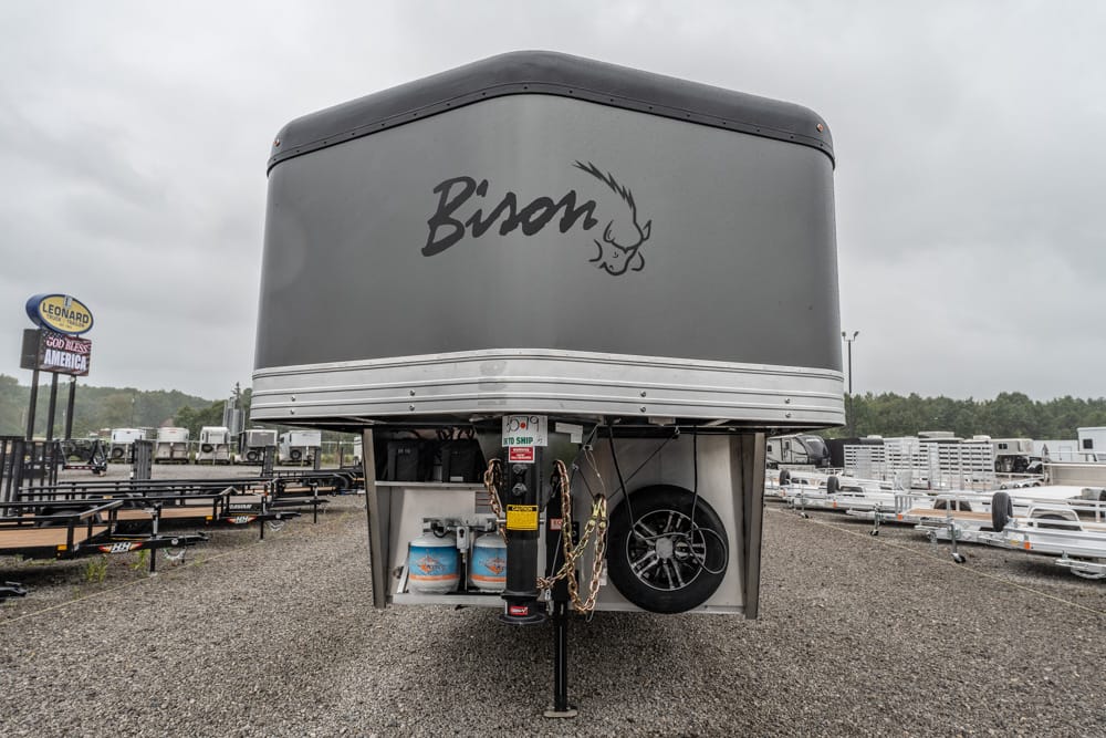 Front view of a large Bison horse trailer in a trailer yard, showing propane tanks, spare tire, and hitch at the gooseneck area.