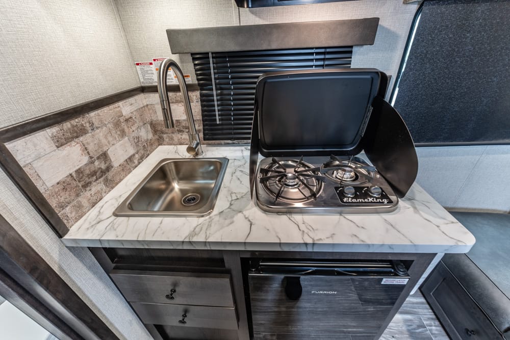 Compact RV kitchenette: stainless steel sink, marble countertop, and a Flame King two-burner stove with lid, all in a small galley.]','Two-burner gas stove with open lid next to a small sink on a marble counter in an RV kitchen.