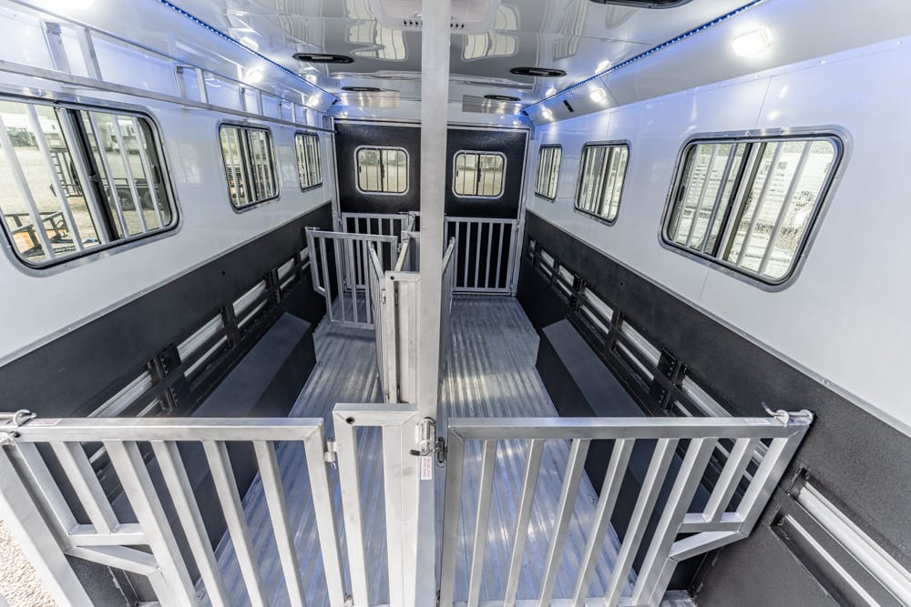 Interior of a metal horse/animal trailer with stalls and dividing gates, side benches, and windows along the walls for ventilation