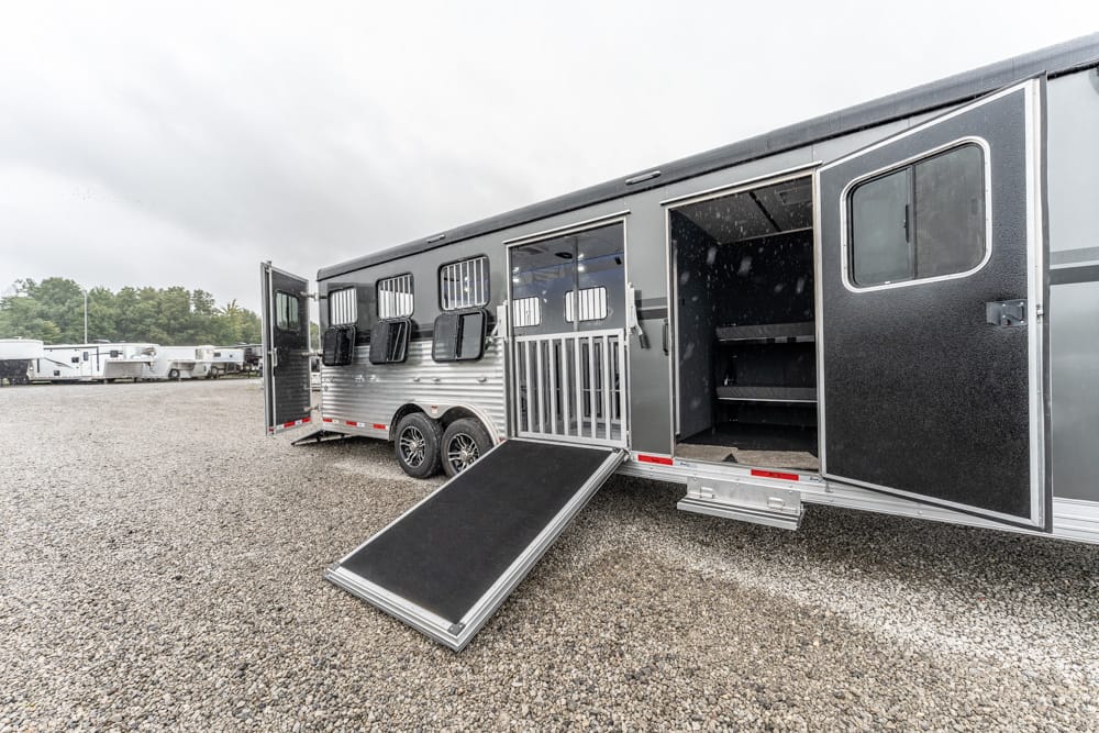 Open horse trailer with ramp down, showing stalls inside on a gravel lot, other trailers in the background