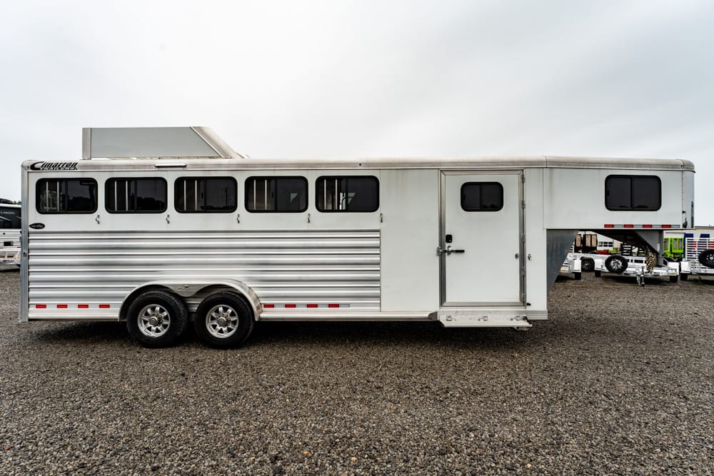 Silver horse trailer with two axles and side windows parked on a gravel lot