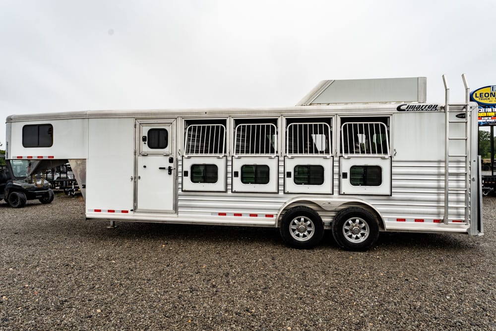 Silver aluminum horse trailer with six stall doors and barred windows, on a gravel lot.