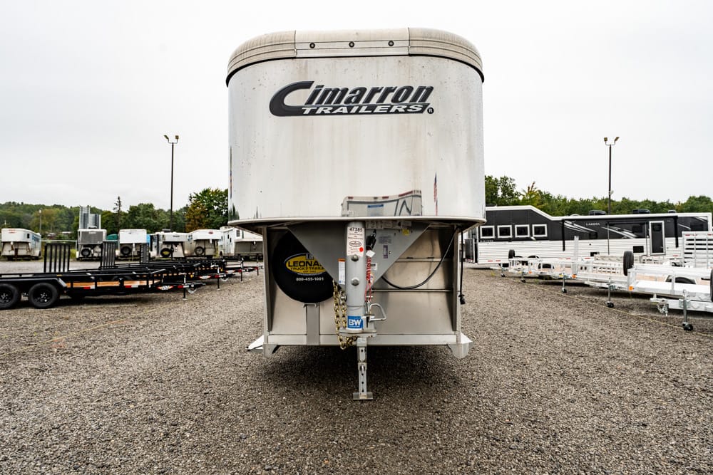 Front view of a large silver Cimarron trailer parked on a gravel lot with other trailers in the background.