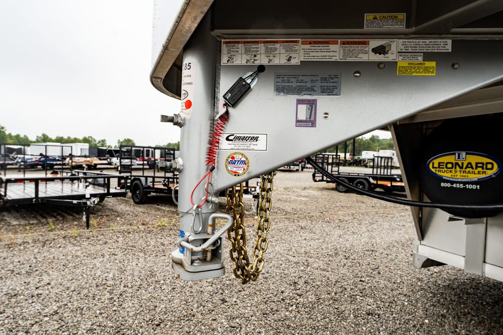 Close-up of a trailer hitch with safety chains and warning labels on a Leonard trailer.