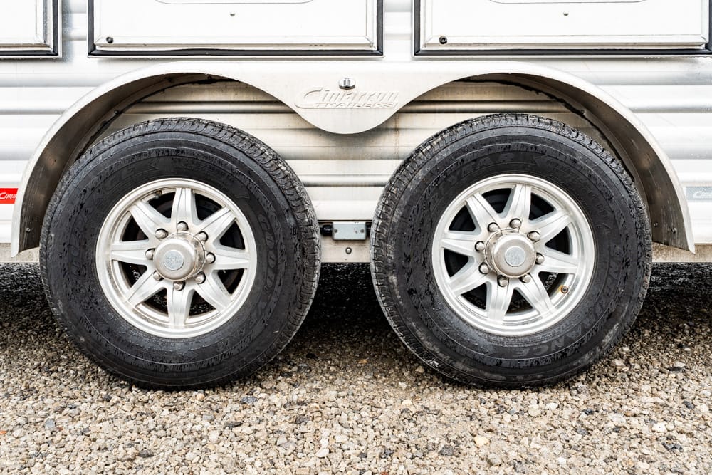 Dual-axle trailer with silver rims and black tires on a gravel surface