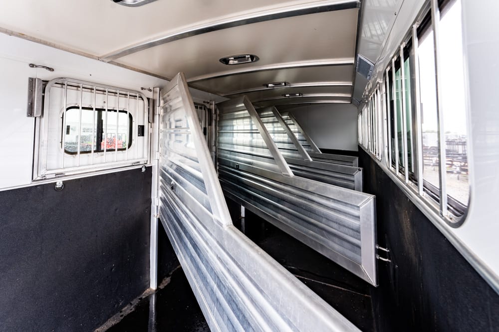 Interior of a metal livestock trailer with angled divider walls creating stalls for animals, metal panels along the sides