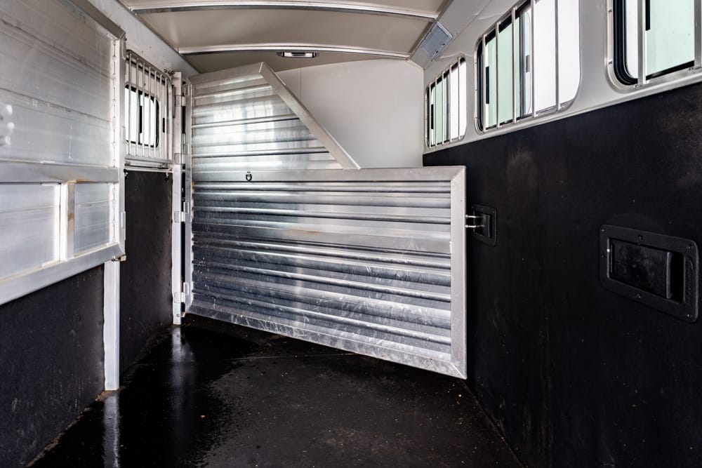 Interior of a metal horse trailer with a corrugated aluminum divider gate, black side walls, and windows along the top.