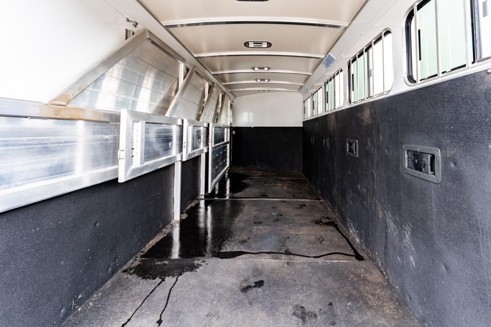 Empty horse trailer interior with metal stall partitions along the left and windows along the right wall