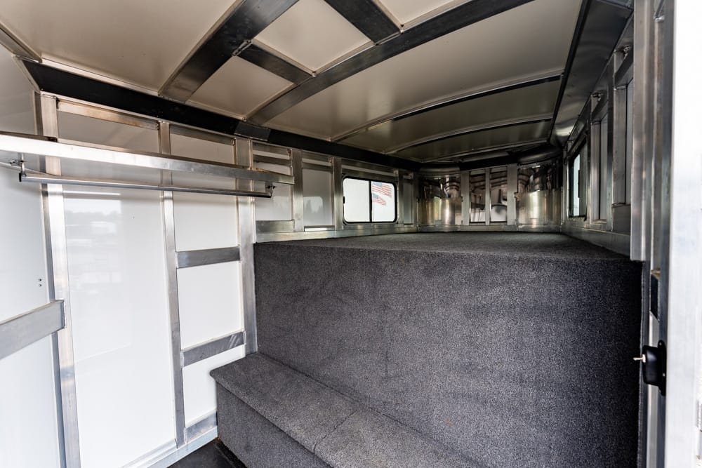 Interior of a cargo trailer with carpeted stairs leading to a raised platform and metal framing along the sides and ceiling.
