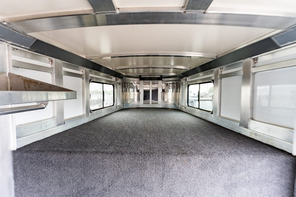 Empty metallic transport car interior with a gray carpet, curved ceiling, and large windows along both sides